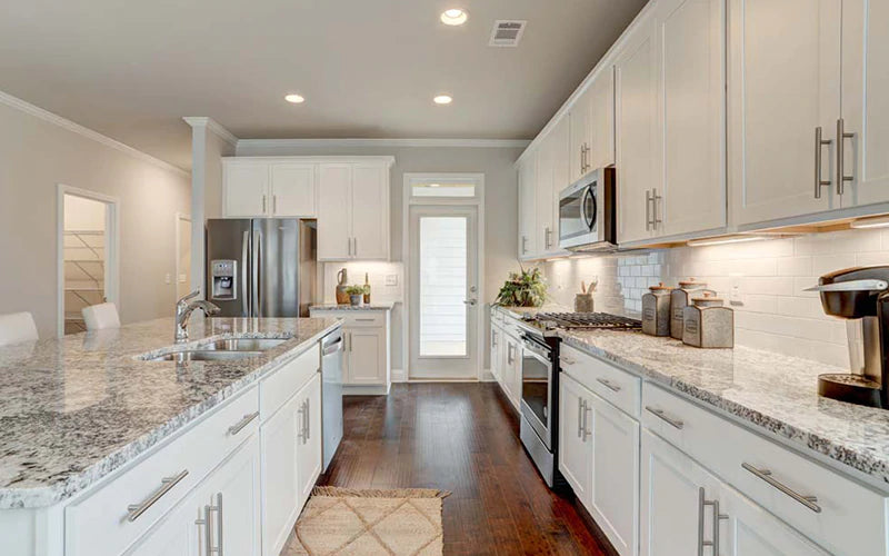Wide view of a kitchen with white cabinets and granite counter tops.